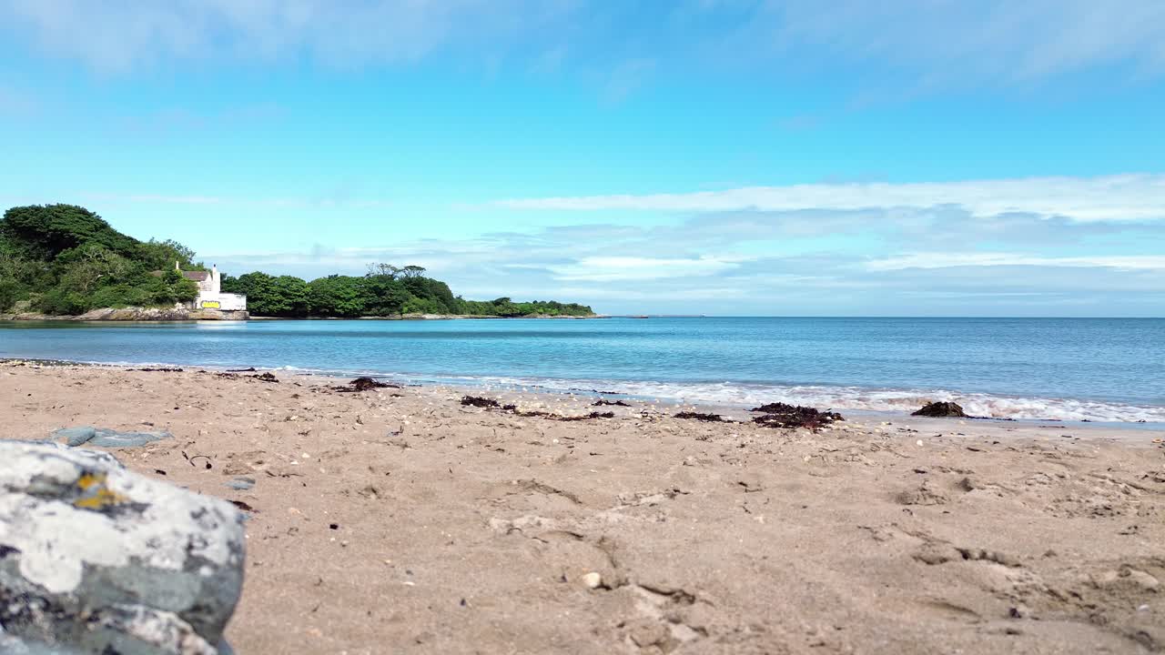 Sea waves washing up on white sandy Welsh Penrhyn secluded beach shoreline under blue sky