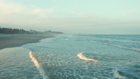 Aerial-drone-flying-over-ocean-coast,-tide-rolling-onto-shore-of-a-luxurious-vacation-home-island