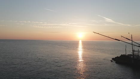 Aerial-view-of-a-trabucco-silhouette,-a-traditional-fishing-machine,-on-the-italian-seashore,-at-sunset