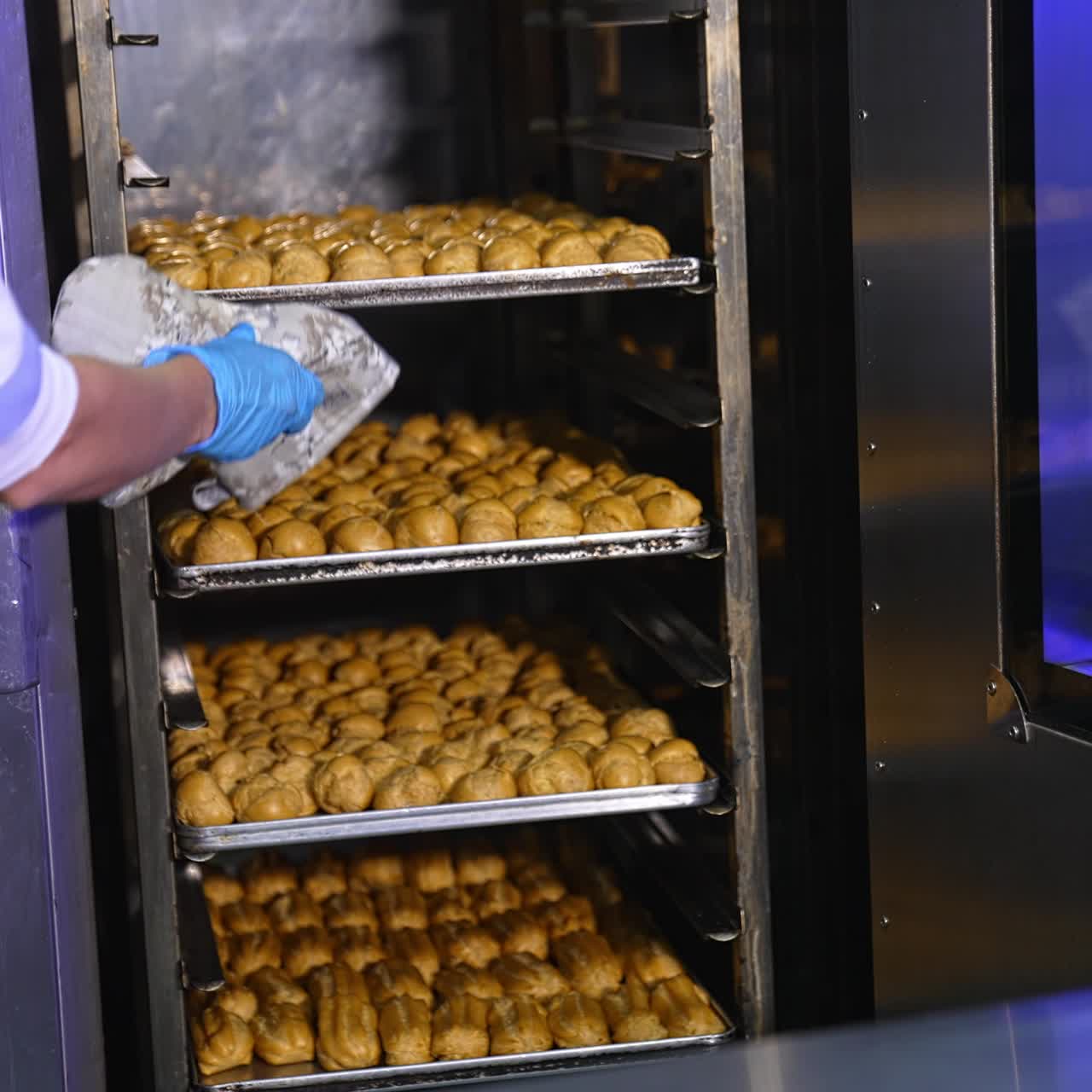 Freshly baked profitroles being taken off the oven. Factory worker pulls the baking sheet from oven and puts it on the table. Close up