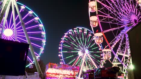 multiple ferris wheels spinning at manufacturer of fairground attractions during nighttime