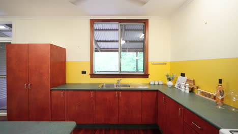 reverse dolly in kitchen walkway of yellow colourful house with wooden floorboard cabinets