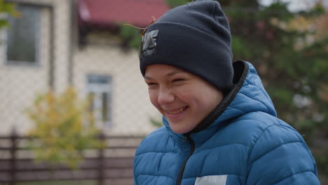 joyful young boy in blue jacket and black beanie, laughing as autumn leaves are playfully thrown at him, with a blurred background