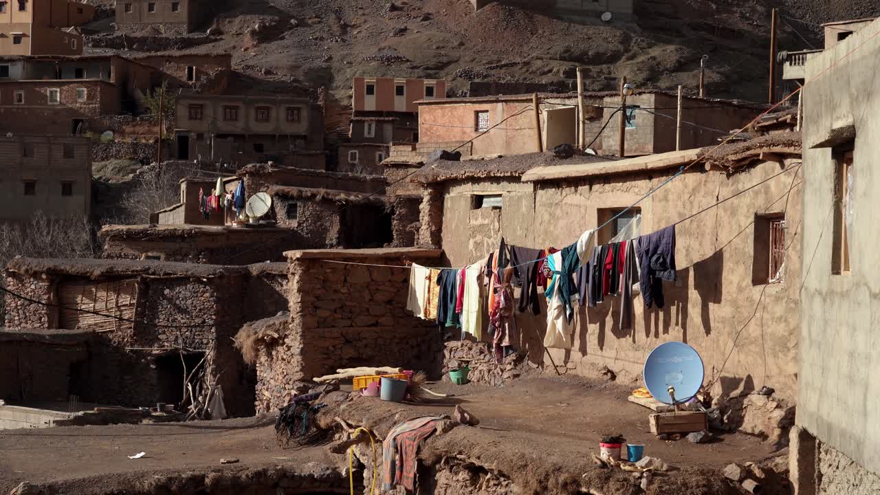 At the edge of the mountain village, stone homes surround a small square where villagers gather, with the imposing Toubkal peaks in Morocco providing a breathtaking view