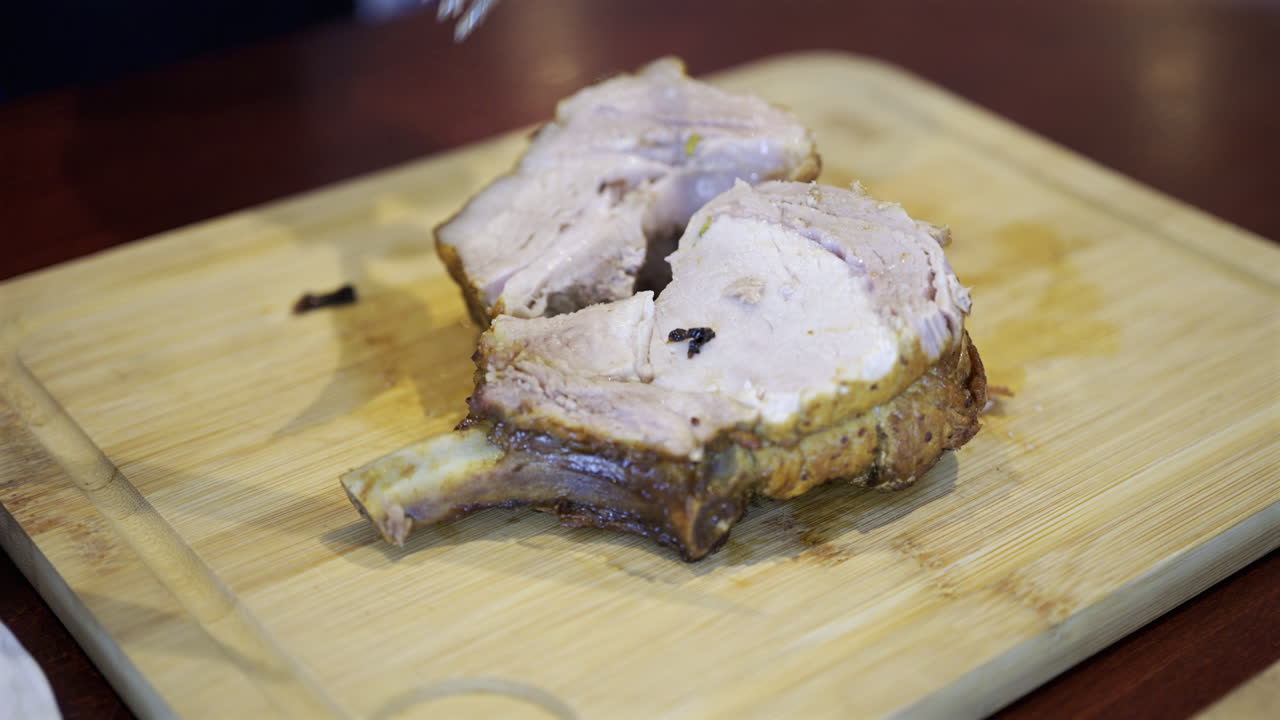Close up of a man's hand cutting up a piece of pork on a wooden tray