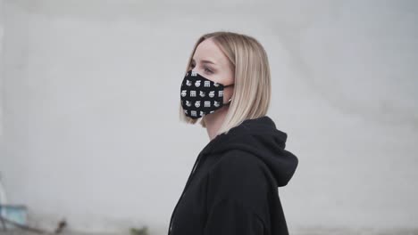 young blonde woman in black clothes and face mask walking in urban exterior