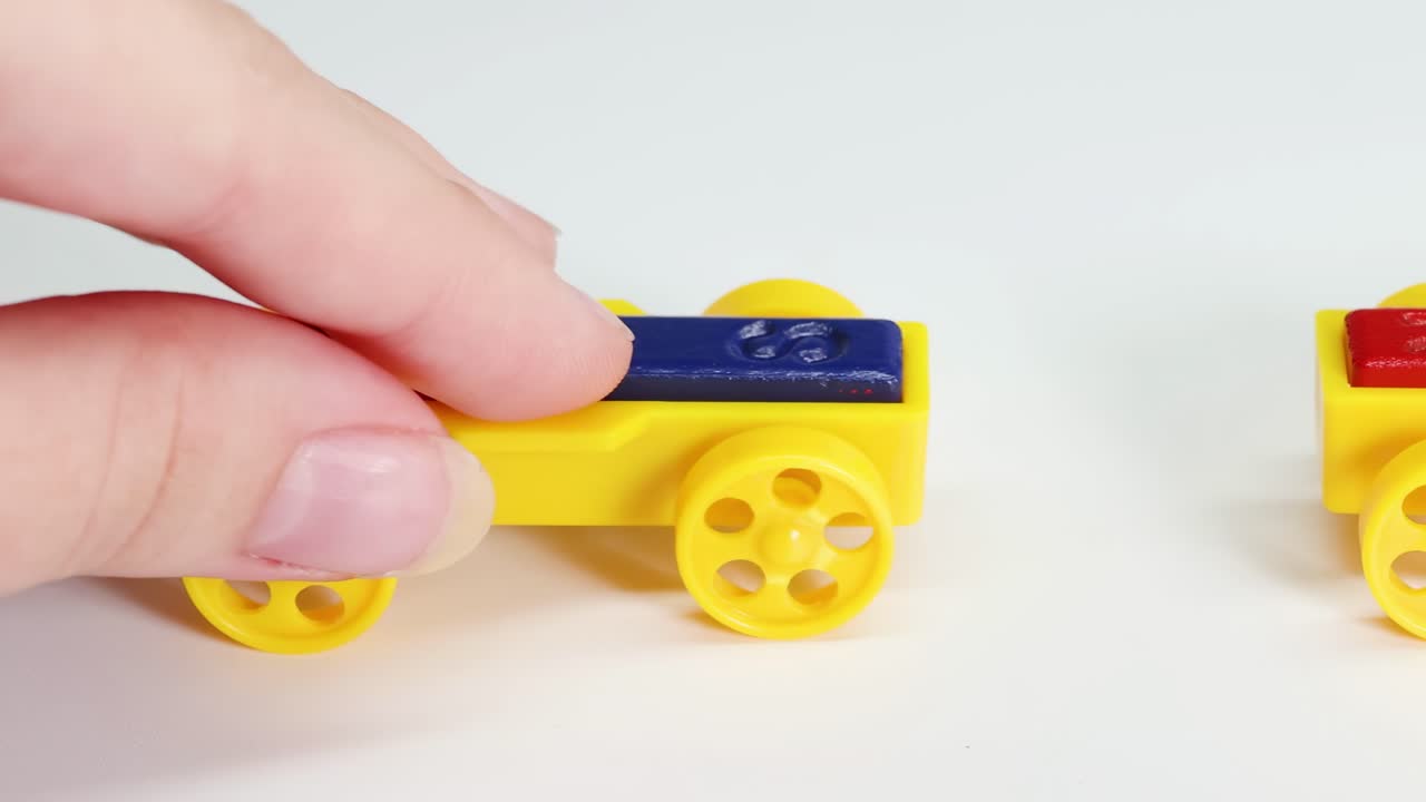 Close-up of hands manipulating yellow toy cars with magnets on a white surface.