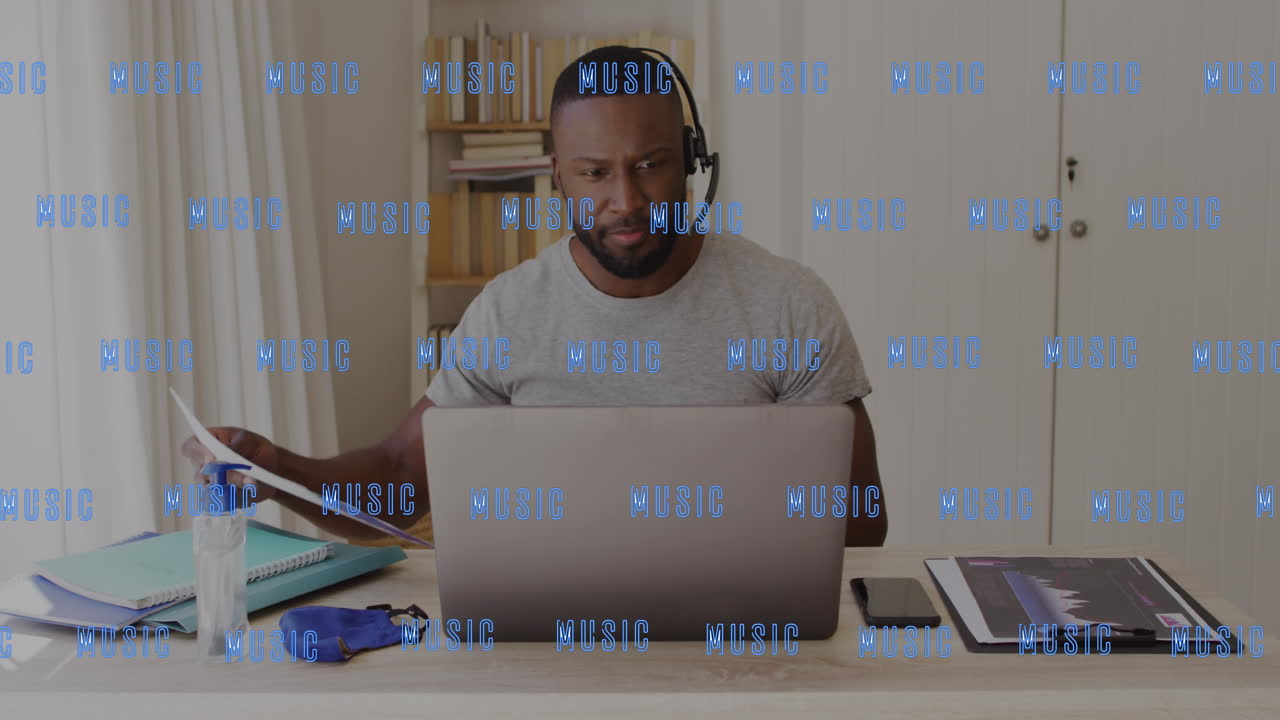 Animation of music text over african american man in phone headset using laptop