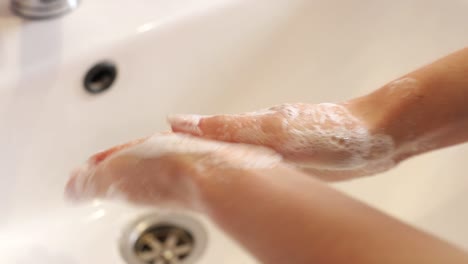 young woman in a red robe washes her hands under running water in a modern bathroom with a round illuminated mirror. high quality 4k footage