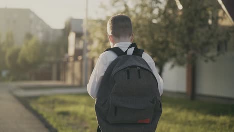 cu tracking back view portrait of schoolboy with knapsack behind his back in school uniform