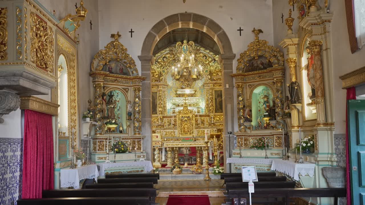 Interno di chiesa cattolica con altare maggiore dorato, altari laterali, banchi e lampadari.