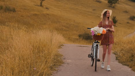 chica de plan medio en vestido va con bicicleta y flores en el campo