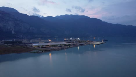 aerial-view-of-Squamish-Spit-conservation-area-harbour-illuminated-at-night,-drone-fly-above-stunning-sunset-seascape