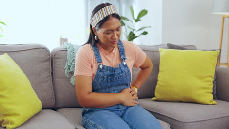 mujer asiática, manos y dolor de estómago en la sala de estar