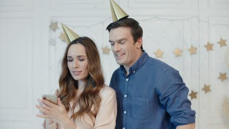 retrato de una pareja feliz haciendo selfie móvil con gorras doradas cerca del árbol de navidad