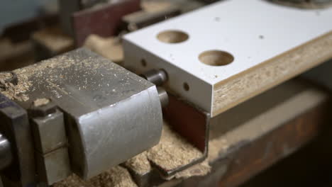 horizontal technical drill bit goes in and out into chipboard wooden element, producing a lot of flying sawdust arround