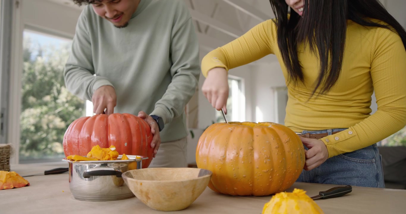 Couple cutting, scooping pumpkins in kitchen after removing lids, ladling pulp into pot for carving
