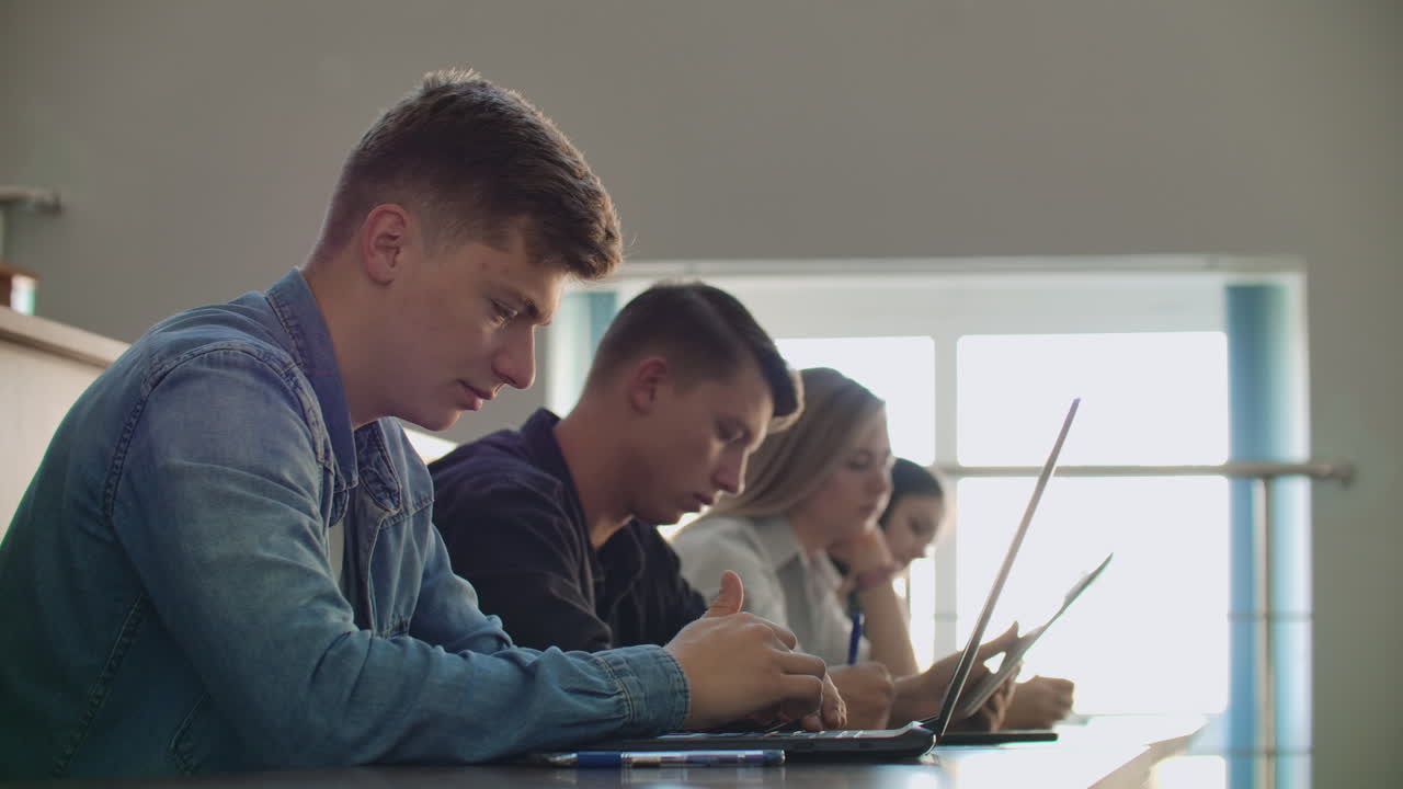 Large Group of Multi Ethnic Students Working on the Laptops while Listening to a Lecture in the Modern Classroom. Bright Young People Study at University.