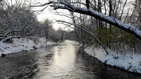 Drone-shot-hovering-over-rushing-river-in-snow-covered-forest-in-Michigan,-USA