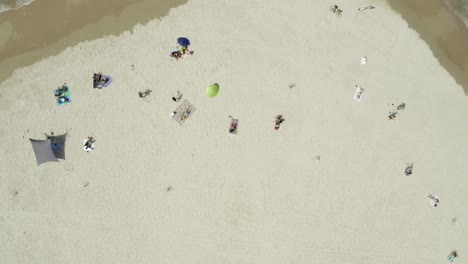 ascending top down drone aerial of tropical beach on a sunny day with many sunbathing people