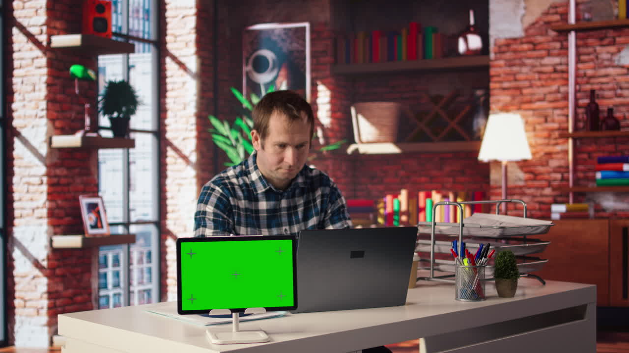 Green screen tablet next to man using laptop, answering phone call