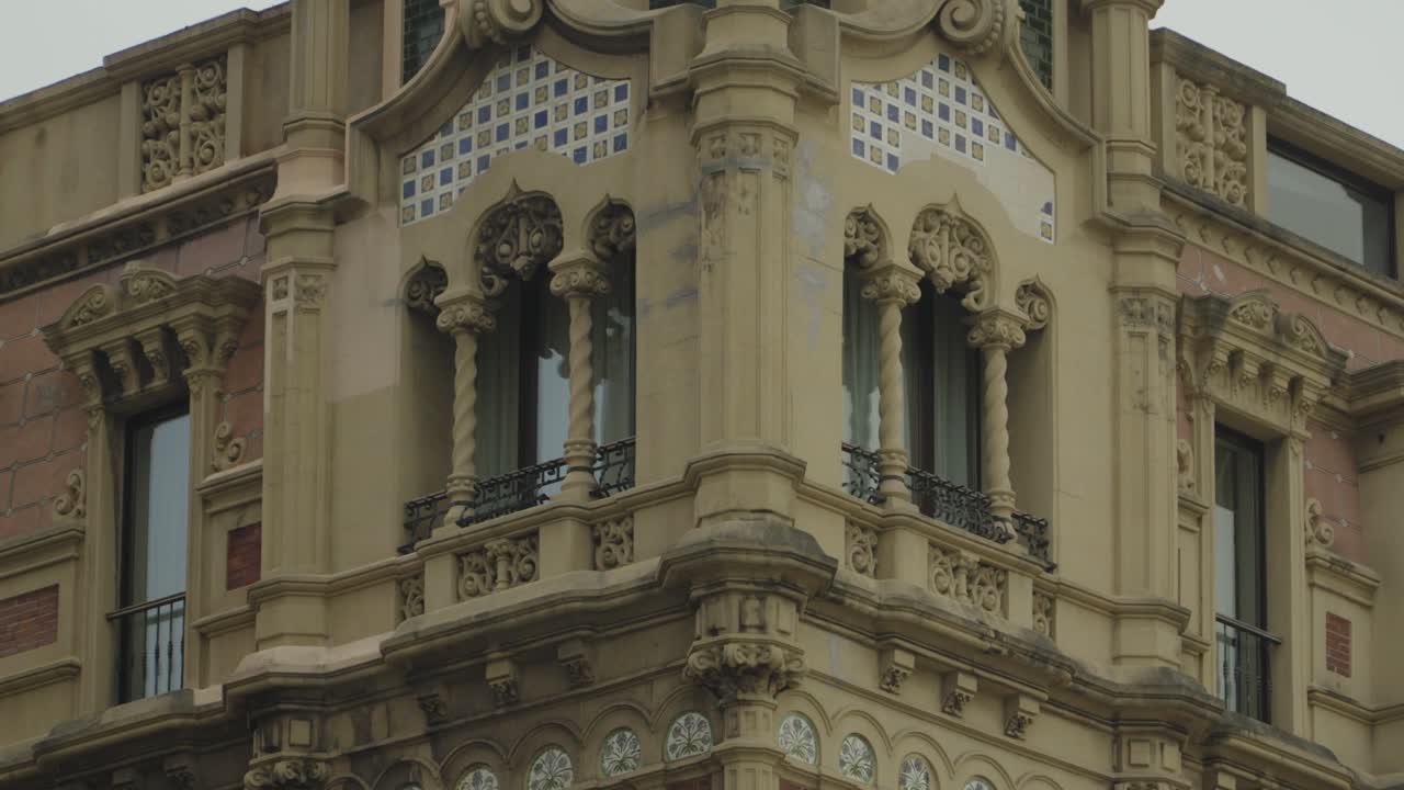 Deslumbrante fachada de edifício de esquina ornamentada em Gijón, Espanha, apresentando entalhes detalhados em pedra, colunas decorativas, varandas de ferro forjado e arquitetura europeia clássica do início do século XX.