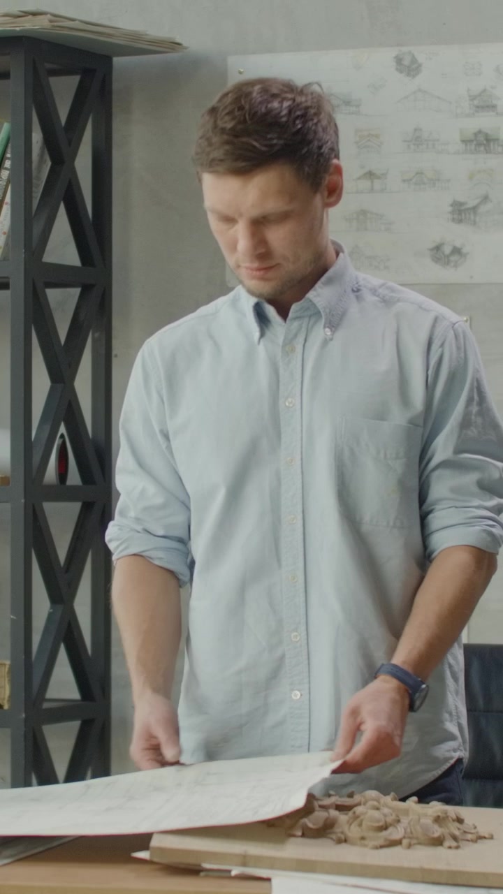 Architect Reviewing Blueprints and Wood Carving in Studio