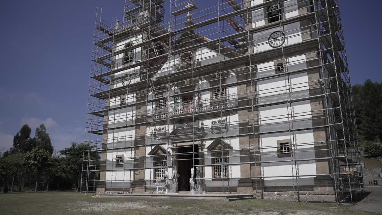 Portuguese church facade surrounded by scaffolding, undergoing restoration under the clear sky