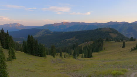 Aerial-of-trees-atop-a-ridge-in-the-Colorado-Rocky-Mountains-with-mountain-range-on-the-horizon-with-a-boom-down-towards-the-ground