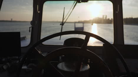 silhouetted view from a ship's bridge with a hand on the helm at sunset