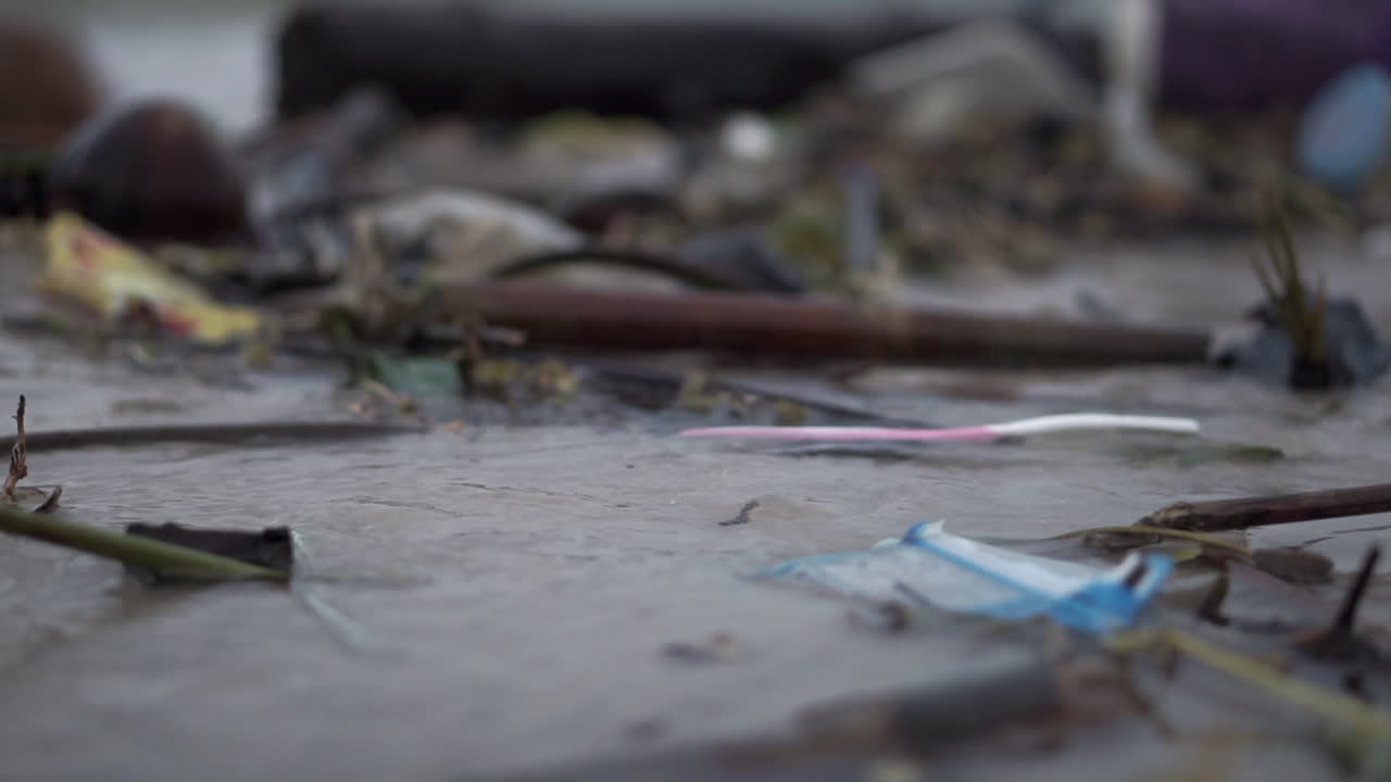 모래와 해안을 따라 물에 플라스틱과 파편으로 가득 찬 매우 오염되고 더러운 해변의 흐름에 떠 있는 플라스틱 칫솔