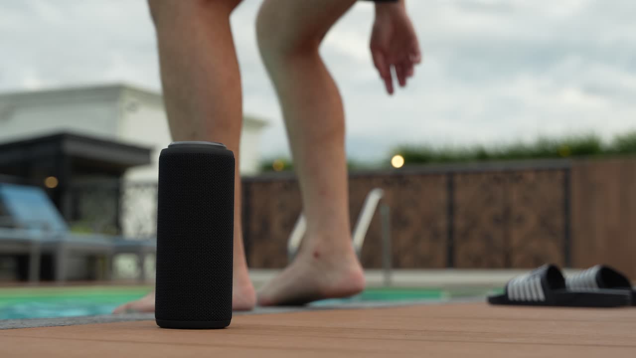 Ragazzo in piscina che si rilassa con la musica dal suo altoparlante Bluetooth al suo fianco.