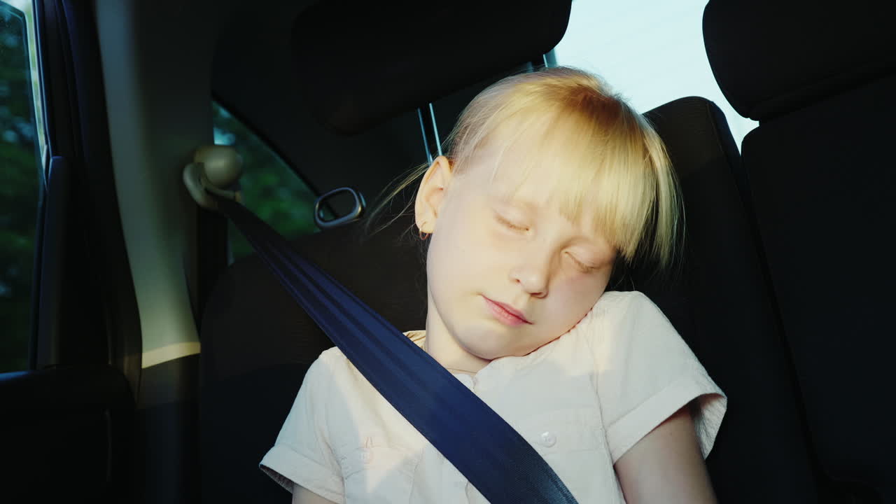 그 소녀는 안전벨트를 매고 차 뒷좌석에 타고 있는 6살이고 위에서 잔다.