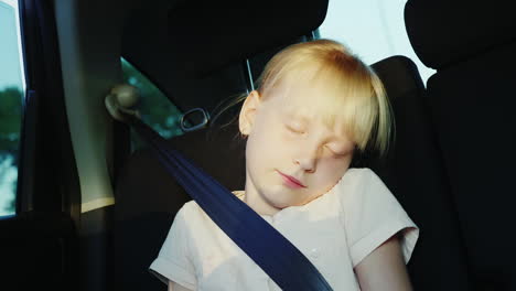 the girl is 6 years old riding in the back seat of the car buckled with a seat belt and sleeps on th