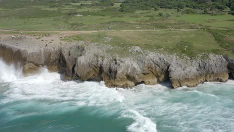 aerial parallax around crashing waves on rocky limestone cliffs, bufones de pria asturias spain, slow motion