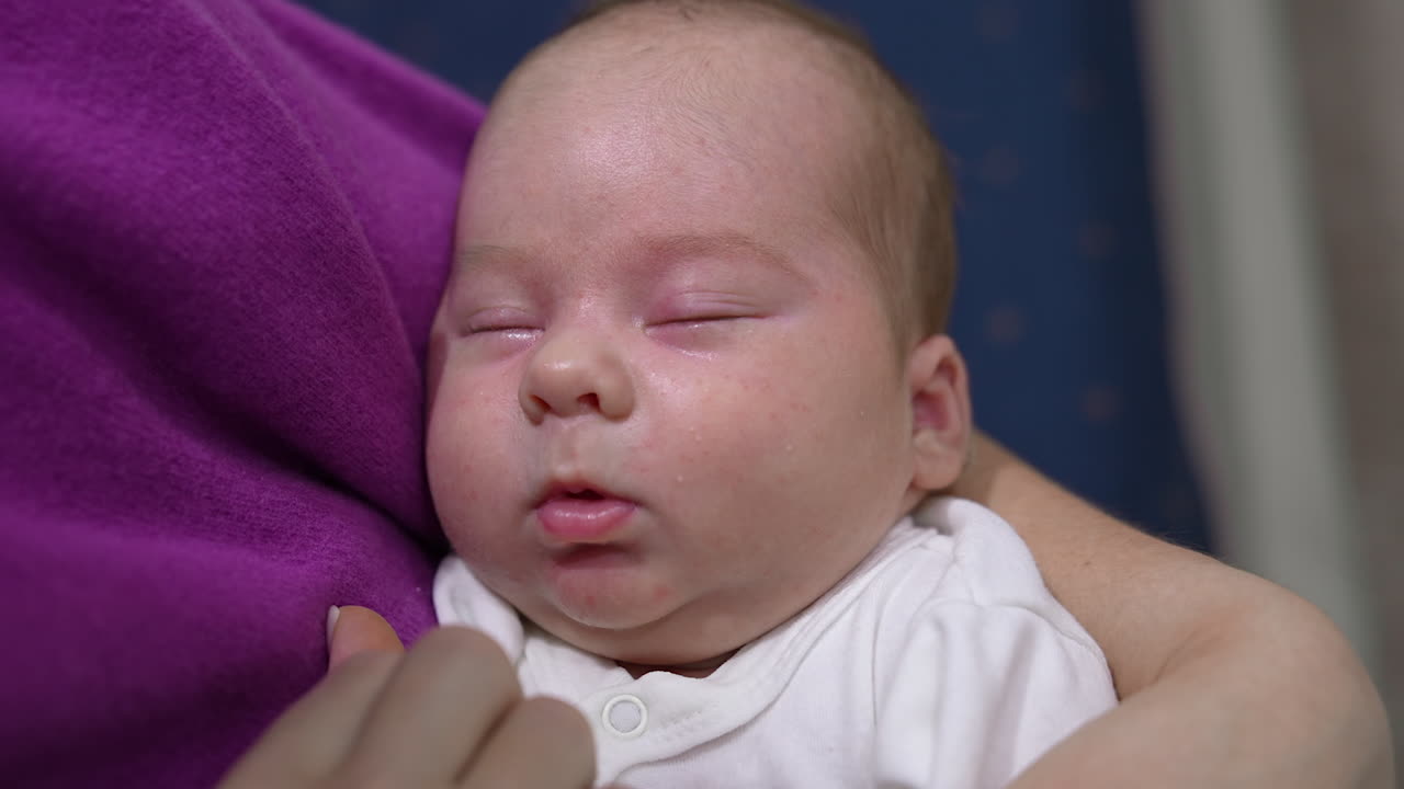 Mother's hand touching her kid's tiny cheeks and nose while the baby is sleeping. Cute baby doesn't want to wake up. Sleeping baby in mother's arms.
