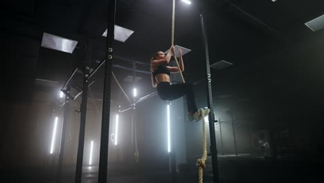 woman is climbing rope in fitness center physical exercise developing endurance and power of arms