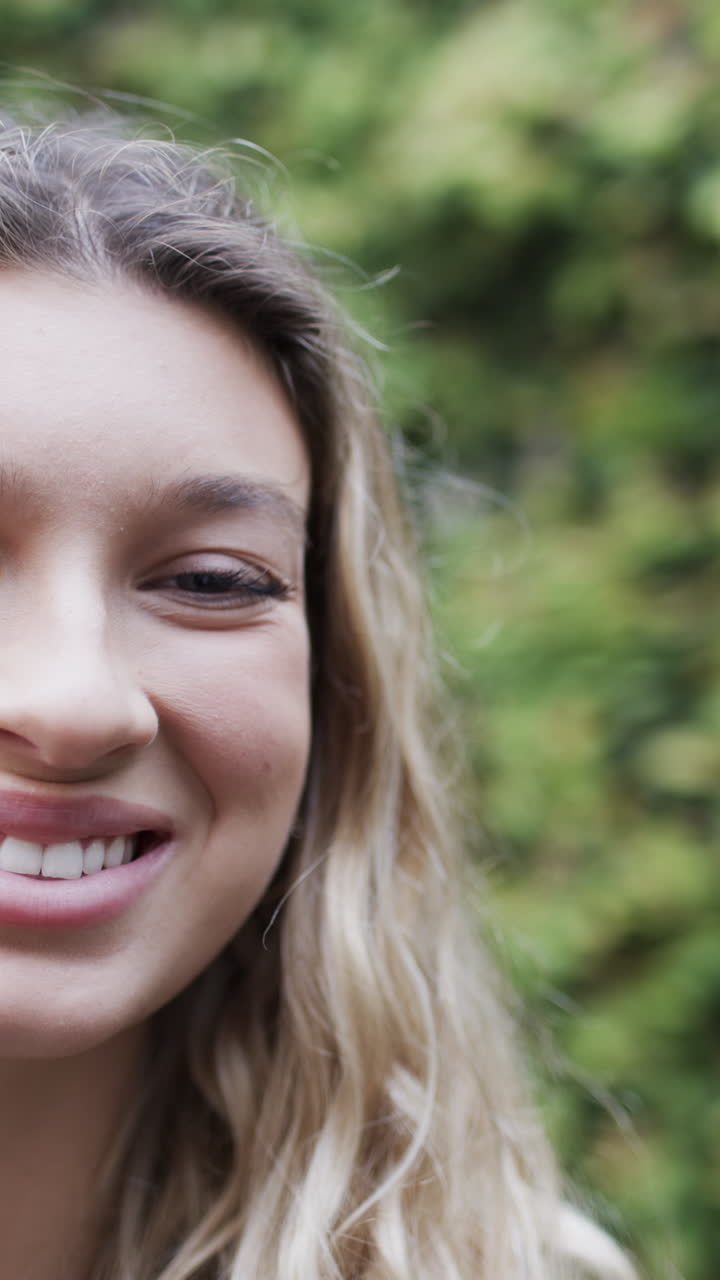 Vertical video of portrait of happy biracial woman smiling in garden, slow motion, copy space
