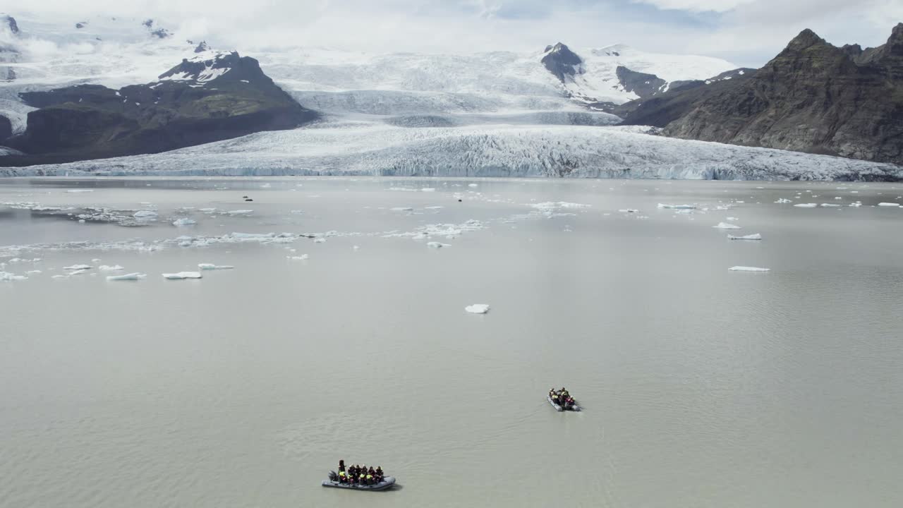 아이슬란드의 빙하 호수에서 떠다니는 사람들과 함께 배경에는 산과 빙하가 있습니다.