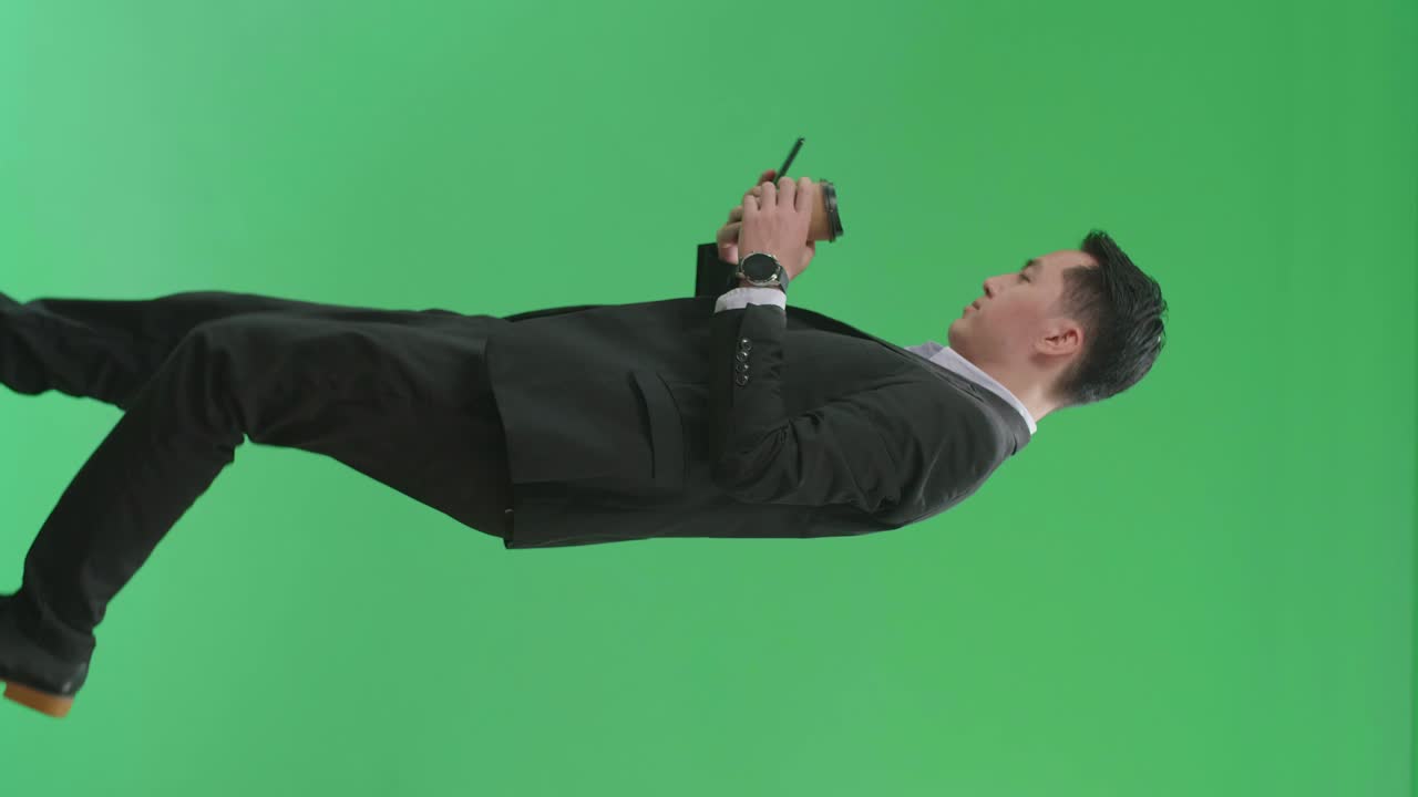 Side View Of Asian Business Man Use Mobile Phone And Drink Coffee While Walking On Green Screen Chroma Key