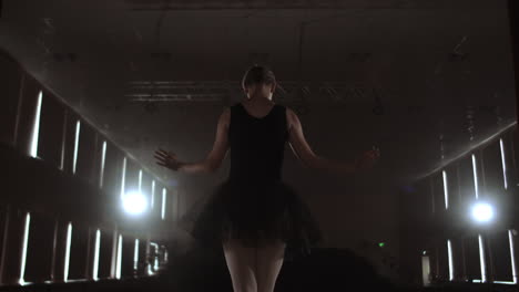 close-up of ballet dancer as she practices exercises on dark stage or studio. ballerina shows classic ballet pas. slow motion. flare gimbal shot.