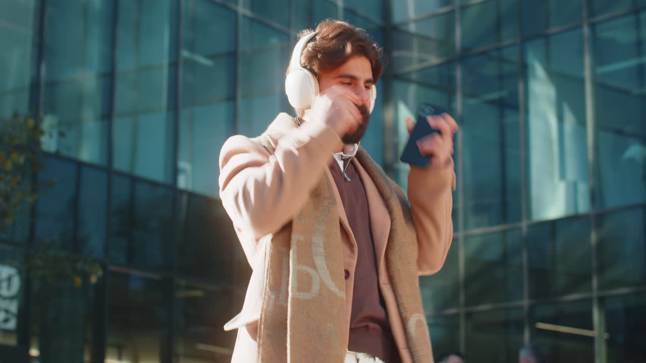 행복한 젊은이가 헤드폰을 착용하고 길거리에서 스마트폰에서 좋아하는 에너지 음악을 듣고 있습니다.