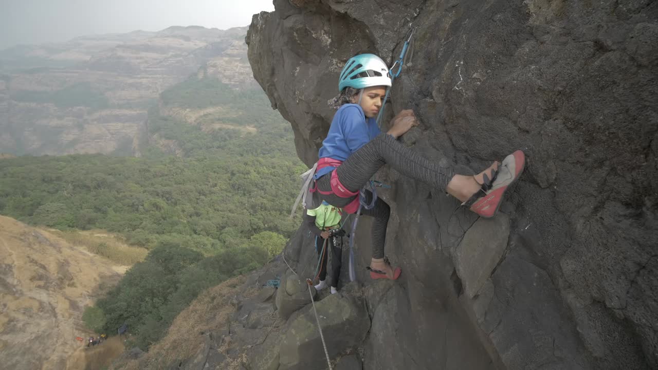 A young Indian girl attempting to rock climb a beautiful pinnacle on sunny day