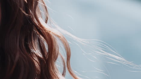 woman with curly red hair waved by light wind at sunlight