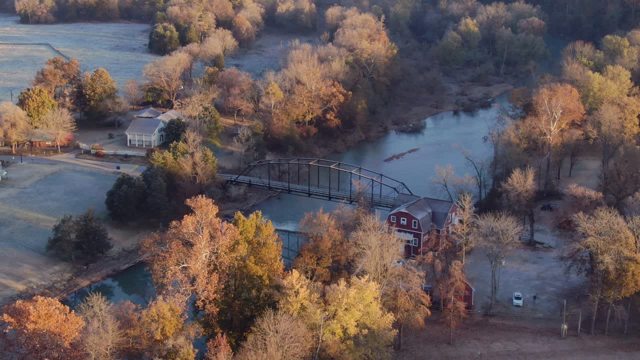 Stationary aerial view of the War Eagle grist mill beside the White river with old iron bridge and farmhouse nestled in the fall colors of the Ozark Mountains