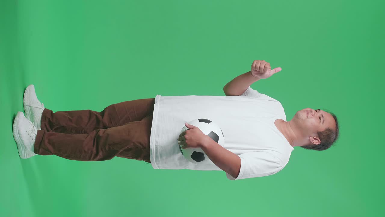 hombre sosteniendo una pelota de fútbol y dando pulgares hacia arriba