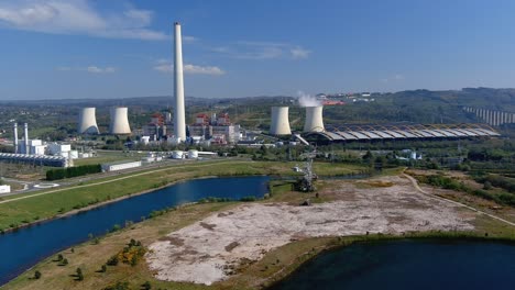 Central-Térmica-Con-Chimenea-Humeante-Detrás-Del-Lago-Y-Un-Viejo-Taladro,-Puente-A-La-Derecha,-Tarde-Luminosa-Y-Soleada.