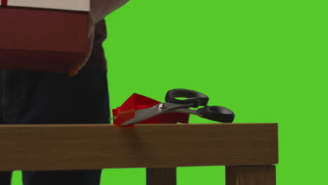 Close-Up-Of-Man-Putting-Down-Gift-Wrapped-Presents-In-Boxes-Decorated-With-Ribbon-On-Table-Shot-Against-Green-Screen-1