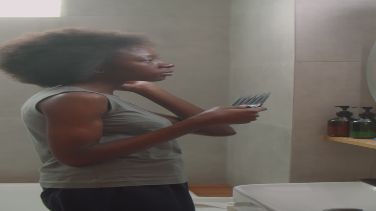 Black Woman Brushing Hair with Comb in Bathroom