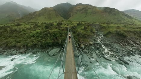 woman hiker with nordic walking poles crossing above rapids on suspension bridge